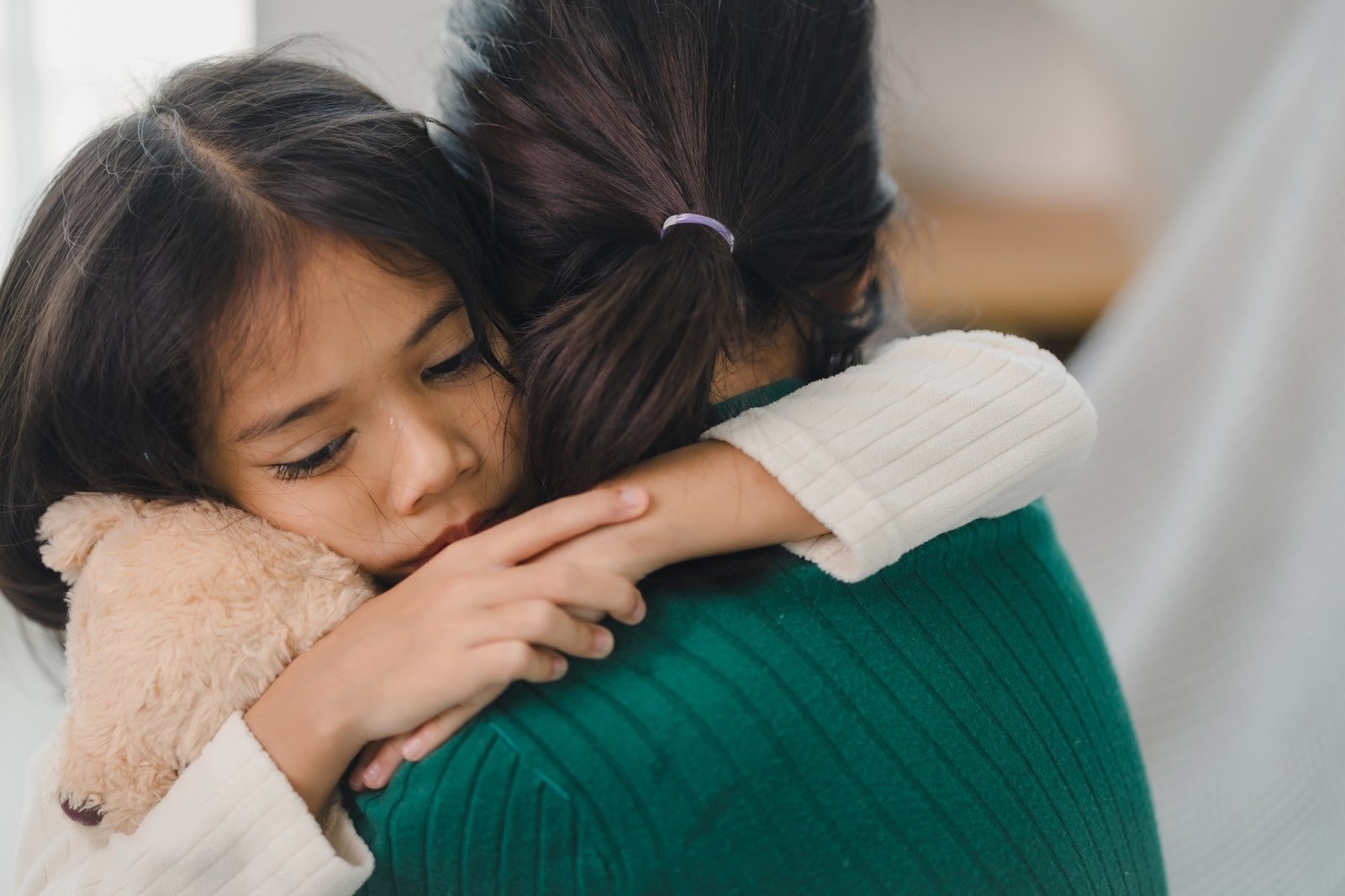 Child hugging an adult while holding a teddy bear, representing emotional safety, support, and healing through connection