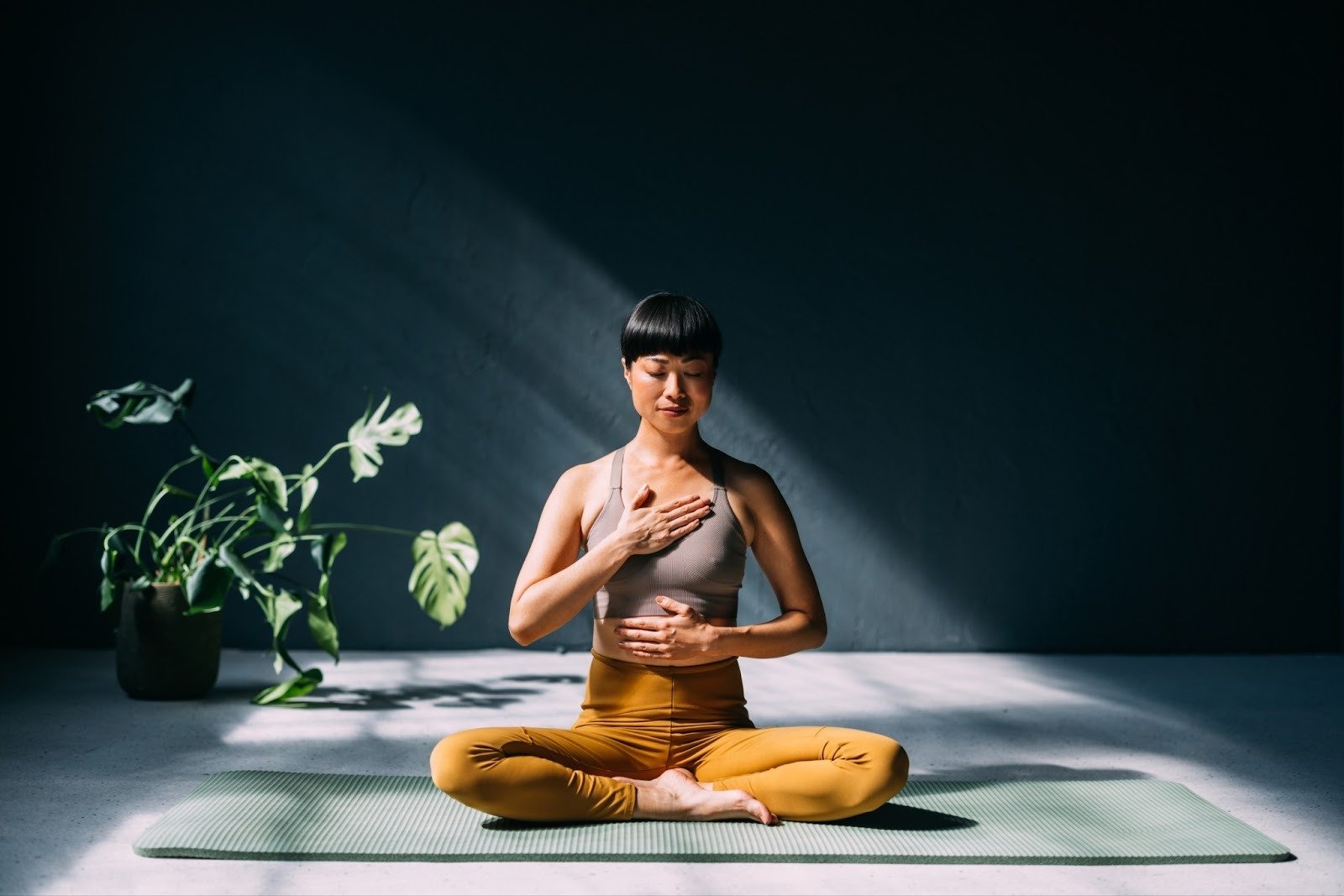 Woman sitting cross-legged on a yoga mat with hands on chest and stomach, practicing mindful breathing to support emotional healing and inner regulation