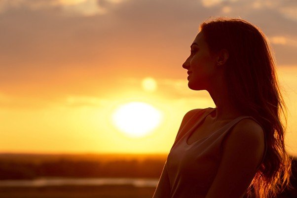 Woman peacefully gazing toward the sunset with warm golden light illuminating her profile.