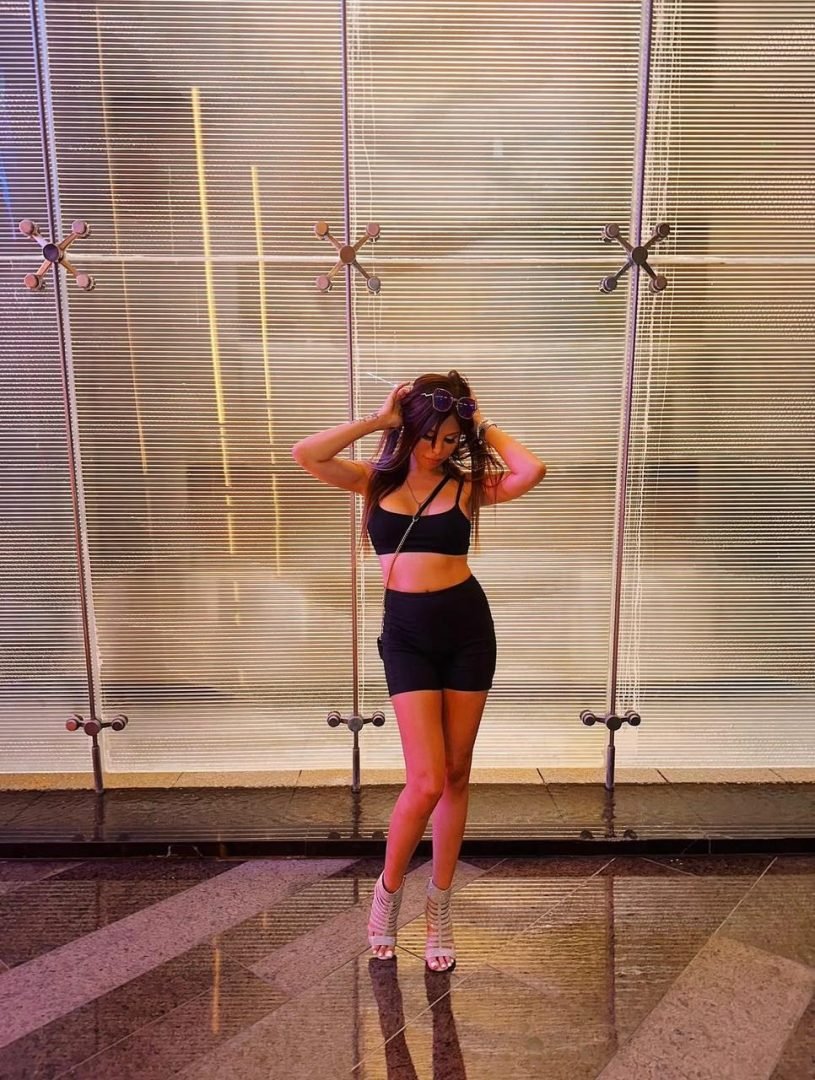 Woman in black athletic outfit posing confidently in front of a modern illuminated glass wall.